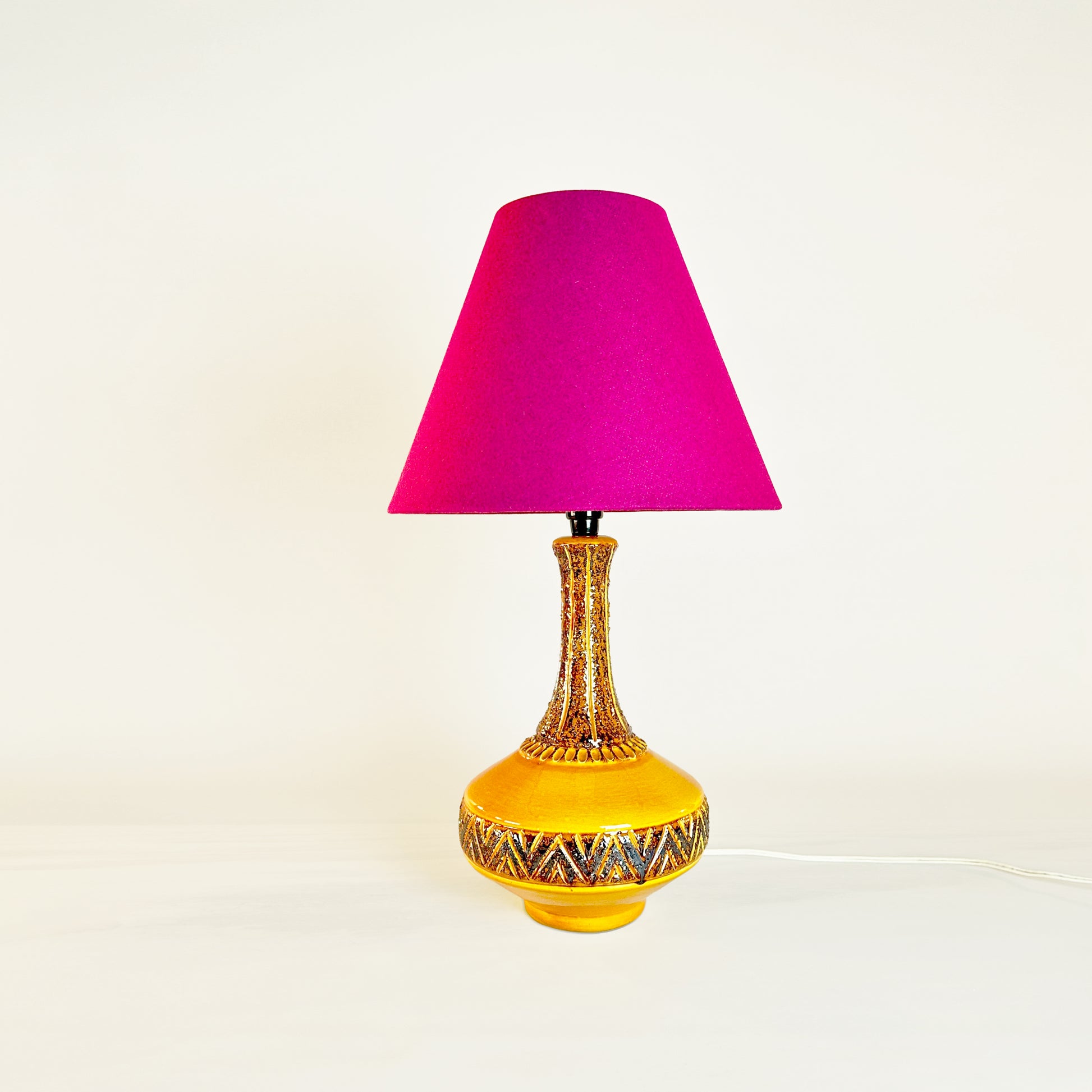 Vintage Mustard Ceramic Glazed Table Lamp, accompanied by a striking Fuchsia empire lampshade An Essence of Timeless Elegance Elevate your space with our stunning Vintage Mustard Ceramic Glazed Table Lamp, a true embodiment of timeless elegance. Paired with a striking Fuchsia empire lampshade, handmade from recycled textured wool. This piece invites a pop of color, a touch of sophistication, and a layer of texture that warmly embraces any space.